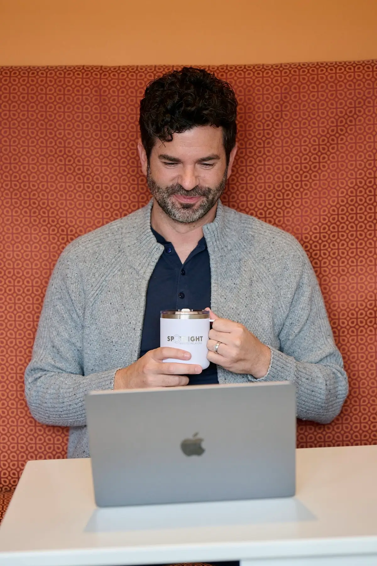 A man holding a coffee cup and looking at a laptop.